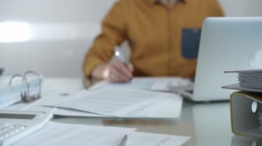 Büyüteç, hesap makinesi, kalem ve belgeler muhasebecilerin masasında yatıyor. Sarı tişört giyen işadamı ya da muhasebeci, arka planda belgelerle çalışıyor. İş adamları, denetim.
