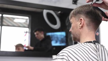 Profesyonel berber, modaya uygun bir berber dükkanında erkek müşterinin saçını ustalıkla kesiyor. Makas ve tarak kullanarak zarif ve modern bir saç kesimi yapıyor.