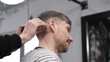 Profesyonel berber, erkek müşterilerin saçlarını makas ve tarakla buduyor. Modern saç stilini modern kuaförde yaratıyor..