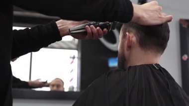 Modern bir berber dükkanında tıraş makinesiyle erkek müşterinin saçını ustalıkla keserek moda ve şık bir saç kesimi yaparak müşterilerin görünüşünü güzelleştiriyor.