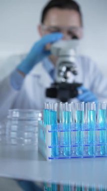 Mavi sıvılı test tüpleri, yakın çekim. Bilim adamı mikroskop kullanarak arka plandaki örnekleri analiz ediyor. Bilim ve Tıp.