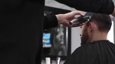 Modern bir berber dükkanında tıraş makinesiyle erkek müşterinin saçını ustalıkla keserek moda ve şık bir saç kesimi yaparak müşterilerin görünüşünü güzelleştiriyor.