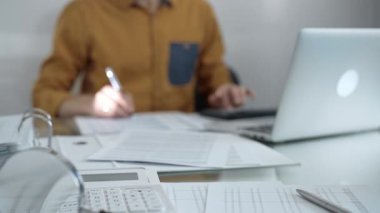Büyüteç, hesap makinesi, kalem ve belgeler muhasebecilerin masasında yatıyor. Sarı tişört giyen işadamı ya da muhasebeci, arka planda belgelerle çalışıyor. İş adamları, denetim.