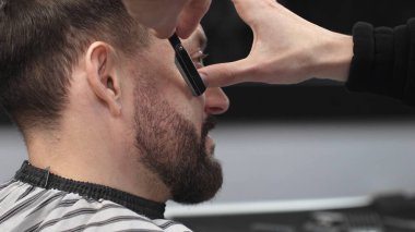 Profesyonel berber, müşterinin sakalını ustura ile dikkatlice tıraş ederek modern bir berber dükkanında kusursuz ve şık bir tımar deneyimi sağlar.