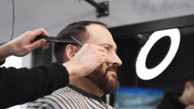 Profesyonel berber, erkek müşterilerin saçlarını makas ve tarakla buduyor. Modern saç stilini modern kuaförde yaratıyor. Yakın plan..