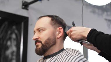 Profesyonel berber elektrikli tıraş makinesi kullanıyor, modern bir berber dükkanında erkek bir müşterinin sakalını titizlikle kesiyor, şık ve parlak bir görünüm çiziyor.