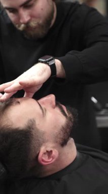 Profesyonel berber müşterilerinin sakallarını ustura ile tıraş eder, jöle sürer ve modern berber ortamında titizlikle bakımı için sıcak havlu kullanır..
