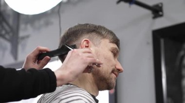Profesyonel berber, erkek müşterilerin saçlarını makas ve tarakla buduyor. Modern saç stilini modern kuaförde yaratıyor..