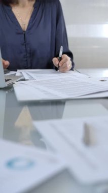 Mavi elbise giyen iş kadını profesyonel ofis ortamında dizüstü bilgisayar, hesap makinesi ve belgelerle çalışıyor. Düşük ışıklandırma, yakın dikey görüntü. İş adamları, denetim kavramı.