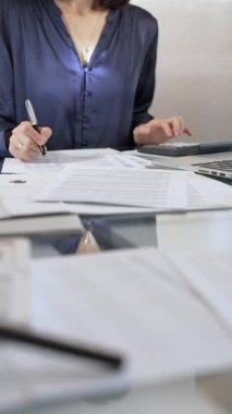 Mavi elbise giyen iş kadını profesyonel ofis ortamında dizüstü bilgisayar, hesap makinesi ve belgelerle çalışıyor. Düşük ışıklandırma, yakın dikey görüntü. İş adamları, denetim kavramı.