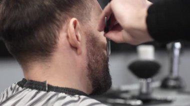 Profesyonel berber, müşterinin sakalını ustura ile dikkatlice tıraş ederek modern bir berber dükkanında kusursuz ve şık bir tımar deneyimi sağlar.