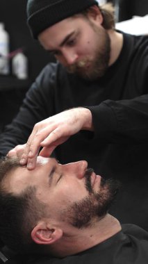 Profesyonel berber müşterilerinin sakallarını ustura ile tıraş eder, jöle sürer ve modern berber ortamında titizlikle bakımı için sıcak havlu kullanır..