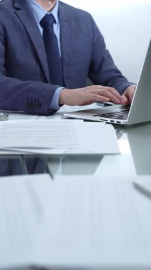 Mavi takım elbiseli iş adamı ofis setindeki cam masada dizüstü bilgisayar, hesap makinesi ve belgelerle çalışıyor. Düşük ışıklandırma, yakın dikey görüntü. İş adamları ve denetim.