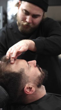 Profesyonel berber müşterilerinin sakallarını ustura ile tıraş eder, jöle sürer ve modern berber ortamında titizlikle bakımı için sıcak havlu kullanır..