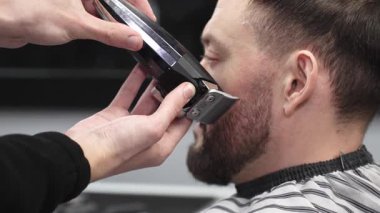 Profesyonel berber, müşterinin sakalını elektrikli jiletle dikkatlice buduyor. Modern bir berber dükkanında kusursuz ve şık bir tımar deneyimi sunuyor.