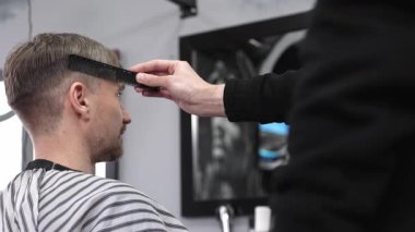 Modern bir berber dükkanında şık bir saç kesimine hazırlanırken müşterinin saçını tarayan profesyonel bir berber.