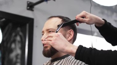 Profesyonel berber, erkek müşterilerin saçlarını makas ve tarakla buduyor. Salonda modern bir saç stili yaratıyor..