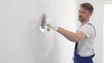 Profesyonel erkek inşaat işçisi, ev yenileme ve iç dekorasyon konusunda uzmanlığını göstermek için duvara alçı yapıştırmak için son bir mala kullanıyor. Dikey görünüm.