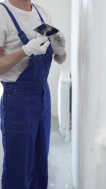 Profesyonel erkek inşaat işçisi, ev yenileme ve iç dekorasyon konusunda uzmanlığını göstermek için duvara alçı yapıştırmak için son bir mala kullanıyor. Dikey görünüm.