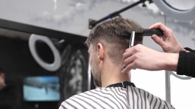 Profesyonel berber, modaya uygun bir berber dükkanında erkek müşterinin saçını ustalıkla kesiyor. Makas ve tarak kullanarak zarif ve modern bir saç kesimi yapıyor.