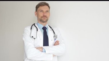 Kendine güvenen erkek doktor kolları çapraz duruyor, steteskop ve beyaz önlük giyiyor. Düşünceli bir şekilde, tıp alanında profesyonelliği ve uzmanlığı somutlaştırıyor. İlaç ve sağlık hizmetleri