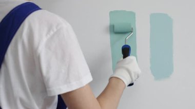 Eldiven giyen ressam beyaz bir duvara boya silindiri uyguluyor, mavi rengin çeşitli tonlarını test ederek iç tasarım için güzel bir eğim etkisi yaratıyor.