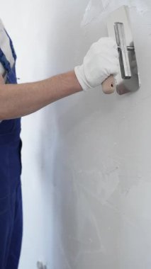 Profesyonel erkek inşaat işçisi, ev yenileme ve iç dekorasyon konusunda uzmanlığını göstermek için duvara alçı yapıştırmak için son bir mala kullanıyor. Dikey görünüm.