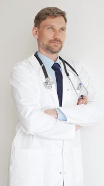 Kendine güvenen erkek doktor kolları çapraz duruyor, steteskop ve beyaz önlük giyiyor. Düşünceli bir şekilde, tıp alanında profesyonelliği ve uzmanlığı somutlaştırıyor. İlaç ve sağlık hizmetleri