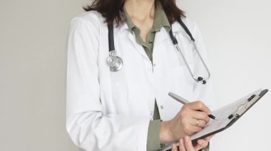 Yeşil bluz üzerine steteskop ve beyaz önlük giyen kimliği belirsiz kadın doktor tıbbi uzmanlığı ve hasta bakımını temsil eden bir panoya yazı yazıyor. İlaç ve sağlık hizmetleri kavramı.