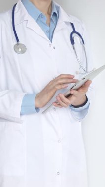 Mavi bluz ve steteskop üzerine beyaz önlük giyen kimliği belirsiz kadın doktor dijital tablet kullanıyor. Bu da tıpta yenilikçi sağlık uygulamaları olduğunu gösteriyor. Sağlık ve Tıp Konsepti.