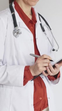 Tuğla kırmızı bluzun üzerine steteskop ve beyaz önlük giyen kimliği belirsiz kadın doktor tıp uzmanlığını ve hasta bakımını temsil eden bir panoya yazı yazıyor. Tıp konsepti.