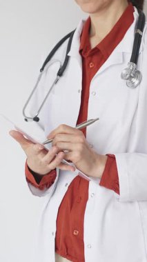 Tuğla kırmızı bluzun üzerine steteskop ve beyaz önlük giyen kimliği belirsiz kadın doktor tıp uzmanlığını ve hasta bakımını temsil eden bir panoya yazı yazıyor. Tıp konsepti.