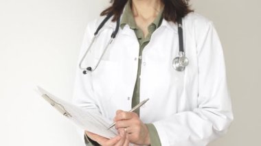 Yeşil bir bluzun üzerine steteskop ve sağlık önlüğü giyen kimliği belirsiz kadın doktor, beyaz bir panoya tıbbi uzmanlığı ve hasta bakımını temsil eden bir yazı yazıyor. Tıp konsepti.