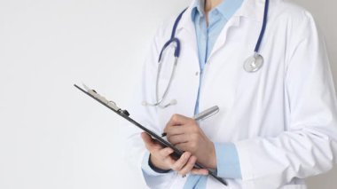 Mavi bluzun üzerine steteskop ve beyaz önlük giyen kimliği belirsiz kadın doktor tıbbi uzmanlığı ve hasta bakımını temsil eden siyah bir panoya yazı yazıyor. Tıp konsepti.