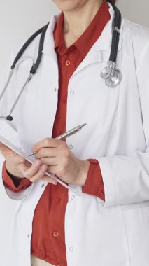 Tuğla kırmızı bluzun üzerine steteskop ve beyaz önlük giyen kimliği belirsiz kadın doktor tıp uzmanlığını ve hasta bakımını temsil eden bir panoya yazı yazıyor. Tıp konsepti.