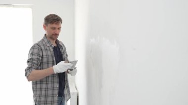 İnşaat işçisi beyaz duvara alçı yayıyor, ev yenileme projesi sırasında koruyucu eldiven takıyor, profesyonel beceri ve odaklanma ile çalışıyor.