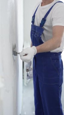 Profesyonel erkek inşaat işçisi, ev yenileme ve iç dekorasyon konusunda uzmanlığını göstermek için duvara alçı yapıştırmak için son bir mala kullanıyor. Dikey görünüm.