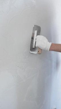 Profesyonel erkek inşaat işçisi, ev yenileme ve iç dekorasyon konusunda uzmanlığını göstermek için duvara alçı yapıştırmak için son bir mala kullanıyor. Dikey görünüm.
