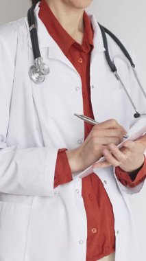 Tuğla kırmızı bluzun üzerine steteskop ve beyaz önlük giyen kimliği belirsiz kadın doktor tıp uzmanlığını ve hasta bakımını temsil eden bir panoya yazı yazıyor. Tıp konsepti.