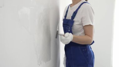 Profesyonel kadın inşaat işçisi, duvarlara alçı yapıştırmak için son malayı kullanıyor. Bu da ev yenileme ve iç dekorasyon konusunda uzman olduğunu gösteriyor..