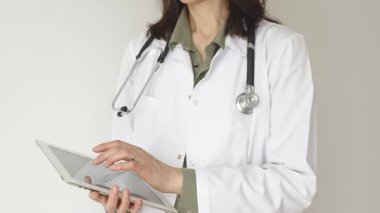 Yeşil bluz ve steteskop üzerine beyaz önlük giyen kimliği belirsiz kadın doktor dijital tablet kullanıyor. Bu da tıpta yenilikçi sağlık uygulamaları olduğunu gösteriyor. Sağlık hizmeti kavramı.
