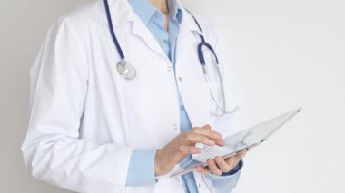 Mavi bluz ve steteskop üzerine beyaz önlük giyen kimliği belirsiz kadın doktor dijital tablet kullanıyor. Bu da tıpta yenilikçi sağlık uygulamaları olduğunu gösteriyor. Sağlık ve Tıp Konsepti.
