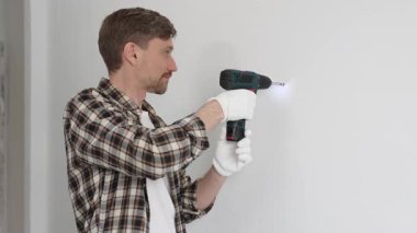 İşaretli gömlek ve güvenlik eldiveni giyen erkek inşaat işçisi, kablosuz tornavida kullanarak duvara vida sokuyor ve dikkatli bir ev tadilatı yapıyor. Dikey görünüm.