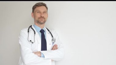 Kendine güvenen erkek doktor kolları çapraz duruyor, steteskop ve beyaz önlük giyiyor. Düşünceli bir şekilde, tıp alanında profesyonelliği ve uzmanlığı somutlaştırıyor. İlaç ve sağlık hizmetleri