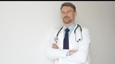 Kendine güvenen erkek doktor kolları çapraz duruyor, steteskop ve beyaz önlük giyiyor. Düşünceli bir şekilde, tıp alanında profesyonelliği ve uzmanlığı somutlaştırıyor. İlaç ve sağlık hizmetleri