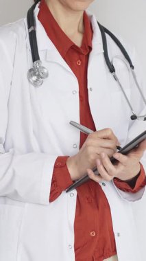 Tuğla kırmızı bluzun üzerine steteskop ve beyaz önlük giyen kimliği belirsiz kadın doktor tıbbi uzmanlığı ve hasta bakımını temsil eden bir panoya yazı yazıyor. İlaç ve sağlık hizmetleri kavramı.