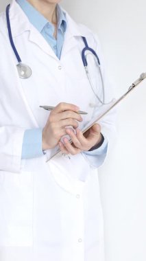 Mavi bluzun üzerine steteskop ve beyaz önlük giyen kimliği belirsiz kadın doktor tıbbi uzmanlığı ve hasta bakımını temsil eden siyah bir panoya yazı yazıyor. Tıp konsepti.