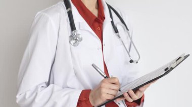 Tuğla kırmızı bluzun üzerine steteskop ve beyaz önlük giyen kimliği belirsiz kadın doktor tıbbi uzmanlığı ve hasta bakımını temsil eden bir panoya yazı yazıyor. İlaç ve sağlık hizmetleri kavramı.