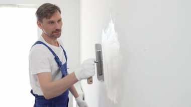 Profesyonel erkek inşaat işçisi, ev yenileme ve iç dekorasyon konusunda uzmanlığını göstermek için duvara alçı yapıştırmak için son bir mala kullanıyor. Dikey görünüm.