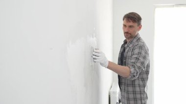 İnşaat işçisi beyaz duvara alçı yayıyor, ev yenileme projesi sırasında koruyucu eldiven takıyor, profesyonel beceri ve odaklanma ile çalışıyor.